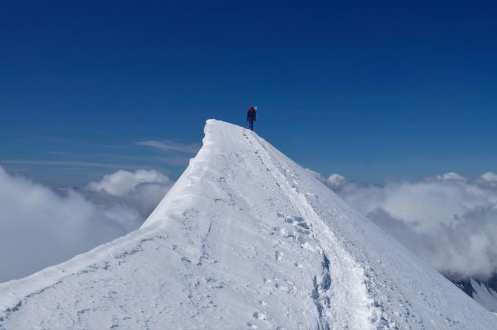 Photo of climber atop a steep, snowy ridge peak